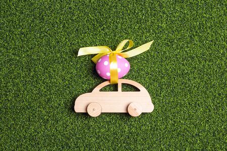 Wooden toy car with Easter egg on the roof  on a green grass background.の写真素材