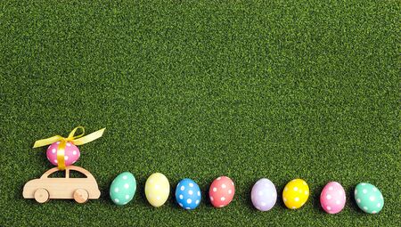 Wooden toy car with Easter egg on the roof and row of eggs on a green grass background. Top view, copy space.の写真素材