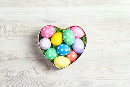 Colored Easter eggs in heart shaped box on light wooden background. Space for text. Top view.の写真素材