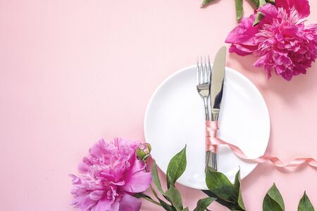 Festive table setting with cutlery and pink peonies  on pink table. Copy space. Top view.