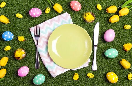 Easter table setting with cutlery, eggs and tulips on a green grass background. Top view, space for text.の写真素材