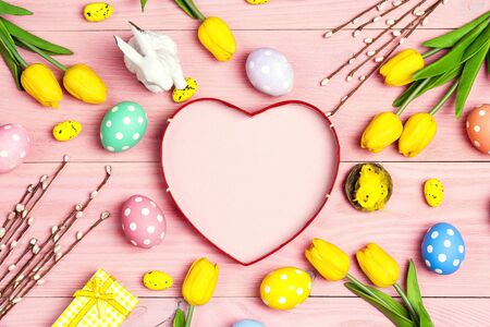 Easter background with eggs, decorations and tulips on pink wooden table. Top down composition with...