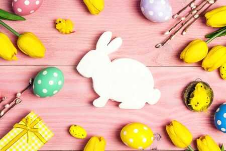 Easter bunny symbol with eggs, decorations and tulips on pink wooden background. Top down...
