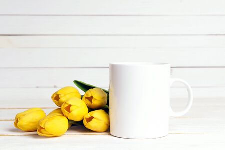 White coffee mug with yellow tulip flowers on white background. Space for text or design.の写真素材