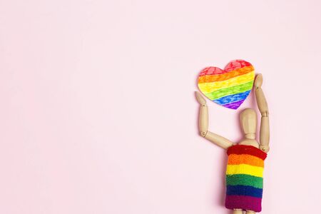 Classic wooden dummy holds lgbt heart on a pink background. LGBT equal rights movement. Space for...