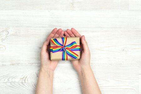 Female hands hold a gift box with rainbow LGBT ribbon on a light wooden table. Homosexual and lgbt concept.の写真素材