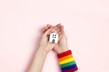 Female hands with lgbt wristband hold a toy house on pink  background. Tolerance to homosexual and bisexual people community concept. Top view, flat lay.の写真素材