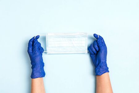 Hands in rubber medical glove with medical face mask on a blue background. Health care and medicine concept.の写真素材