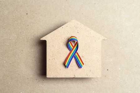 Wooden house silhouette with lgbt rainbow ribbon on brown cardboard background. Symbol of free love and tolerance to homosexual and bisexual people community. Top view.の写真素材
