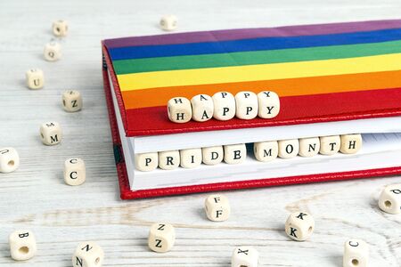 Happy pride month written in wooden blocks in red notebook with rainbow LGBT flag on wooden table. LGBT Pride Month in June.の写真素材