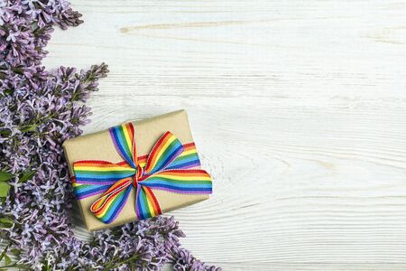 Gift box with rainbow LGBT ribbon and lilac flowers on a light wooden background. Copy space for text. Homosexual and lgbt concept.の写真素材