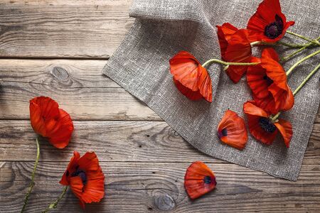 Red poppies flowers with burlap napkin on wooden table. Top view with copy space.の写真素材