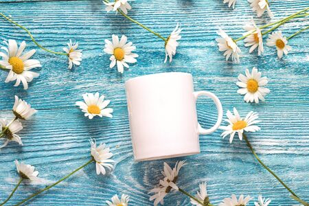 White coffee mug with chamomile flowers on blue wooden background. Space for text or design. の写真素材