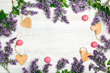 Frame of lilac flowers, hearts and macaroon cookies on light wooden background. Top view, flat lay, copy space.の写真素材