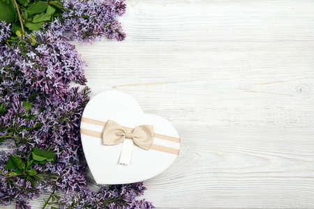 Heart shaped gift box with lilac flowers on light wooden background. Top view with copy space. Spring flowers.の写真素材
