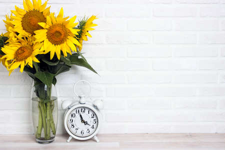 A bouquet of sunflowers in a vase and vintage alarm clock against the white brick wall. Copy space...