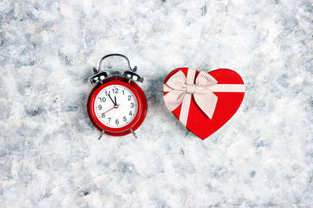 Red classic alarm clock and heart gift box on a gray canvas background. Top view. Valentine's day...