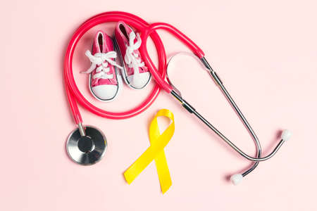 Childhood Cancer Awareness Golden Ribbon with blue baby sneakers and stethoscope on pink background with copy space. Childhood Cancer Day February, 15.の写真素材