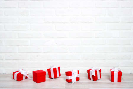 Red gift boxes with white ribbon on a table against the white brick wall. Copy space for text....