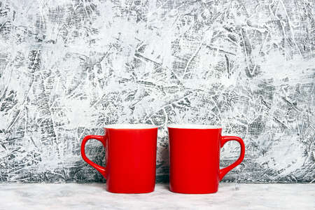 Two red coffee mugs against a gray plaster wall. Place for text or design.の写真素材