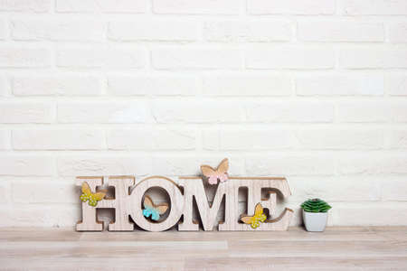 The word HOME with a houseplant on the floor against a white brick wall background. Copy spacefor text.の写真素材