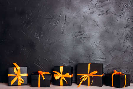 Black gift boxes with orange ribbons on a black background with copy space. Halloween holiday...