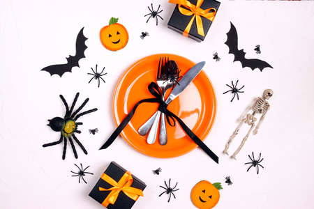 Halloween table setting with orange plate, cutlery, spooky decorations and gifts on white table. Top down composition.の写真素材