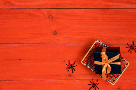 Miniature shopping basket with gift and spider on orange wooden background. Halloween discounts, shopping and sale concept.の写真素材