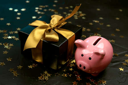 Black gift box with gold ribbon and piggy bank on a black background. Holiday or black friday concept.の写真素材