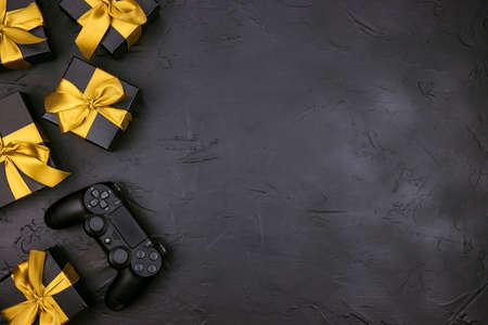 Black background with joystick gaming controller and gift boxes with gold ribbon. Holiday sale or...