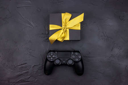 Joystick gaming controller and gift box with gold ribbon on black background. Holiday sale or black...