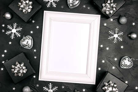 Empty white frame with silver Christmas decorations on a black background with copy space for text. Top view, flat layer.の写真素材
