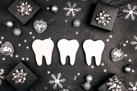 White teeth with silver decorations and gift boxes on black background. Dentist Merry Christmas and New Year concept. Top view, flat lay.の写真素材