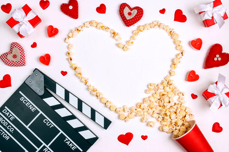Movie clapper board, popcorn heart, gifts and candles on white background with copy space. Valentine's Day, date and romantic evening concept. Love story movies.の写真素材