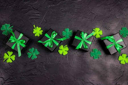 Saint Patrick's Day concept. Decorative clover leaves witn gift boxes on black background. Top down...