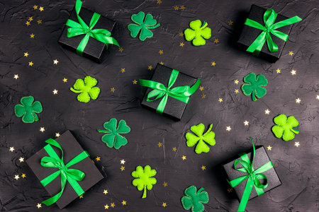 Saint Patrick's Day background with decorative clover leaves witn gift boxes and stars on black. Top down flat lay composition.の写真素材