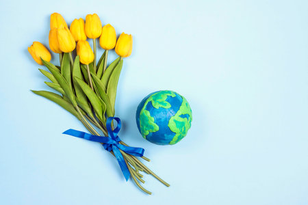Planet Earth with a bouquet of yellow tulips on a blue background. Copy space for text. Earth Day, ecology and nature protect.の写真素材