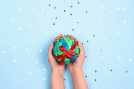 Female hands holding planet Earth with red ribbon among the stars on a blue background. Ecology, environmental protection. World Earth Day concept.の写真素材
