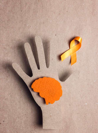 World Multiple Sclerosis Day. Orange awareness ribbon with hand silhouette and brain symbol on a brown background. Copy space for text.の写真素材