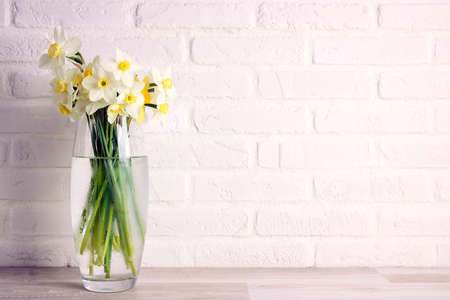 Yellow daffodils in a glass vase against a white brick wall. Copy space. Spring holidays, Mothers Day, Easter concept.の写真素材