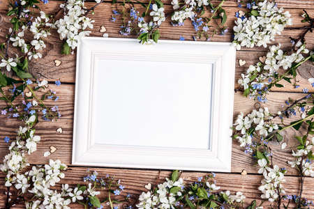 Empty white frame with apple blossom and forget-me-nots on old wooden boards. Top view with copy space for text.の写真素材