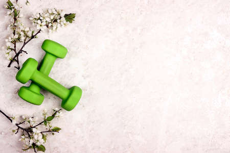 Green dumbbell with apple blossom branches on a light marble background. Top view with copy space.