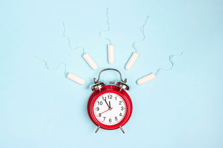 Ringing red alarm clock with sanitary female tampons on blue background. Menstruation cycle period, woman hygiene.の写真素材
