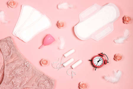 Women's panties with sanitary napkins, tampons, menstrual cup, flowers and feathers on pink background. Different types of feminine hygiene products. Menstruation and feminine hygiene conceot.の写真素材