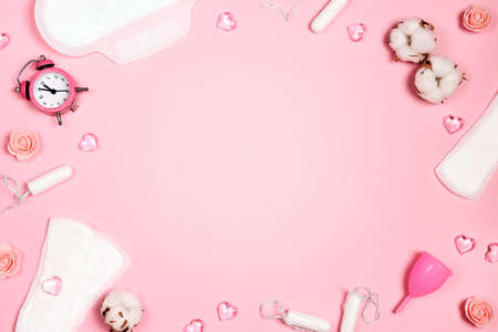 Frame from women's sanitary napkins, tampons, menstrual cup, hearts and flowers on pink background. Different types of feminine hygiene products. Copy space for text.の写真素材