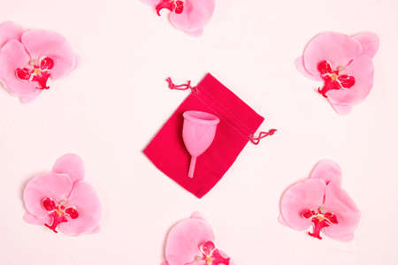Menstrual cup surrounded by orchid flowers on a white background. Women's health, hygiene concept.