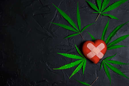 Heart with adhesive plaster and marijuana leaves on black background with copy space. Use of medical marijuana in cardiology.の写真素材