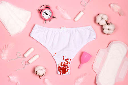 Women's panties with sanitary napkins, tampons, menstrual cup, cotton and feathers on pink background. Different types of feminine hygiene products. Menstruation and feminine hygiene conceot.の写真素材