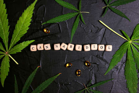 Word Cannabidiol with oil capsules and marijuana leaves on black background. Health care with hemp oil concept.の写真素材