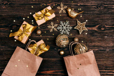Brown paper shopping bags with gold Christmas decorations and gifts on wooden background. Top down...